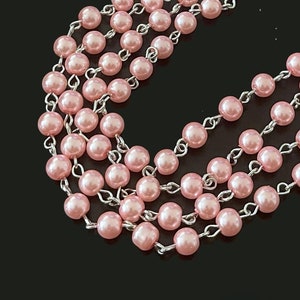 May include: A strand of pink pearl beads strung on a silver chain. The beads are small and round, and the chain is delicate.