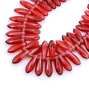 May include: A strand of translucent red glass beads shaped like elongated teardrops or petals. The beads are arranged in a continuous loop, showcasing a vibrant crimson hue and a smooth, polished finish that reflects light across their surfaces.