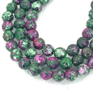 May include: A strand of green and pink faceted gemstone beads. The beads are round and have a rough, textured surface.