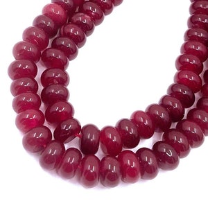 May include: Strands of polished, deep red beads. The beads are round and evenly sized, strung together to form a necklace or bracelet. The beads have a glossy finish and reflect light, creating a vibrant appearance. The background is plain white.