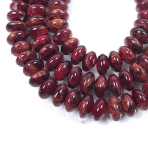 May include: A strand of red and gold oval-shaped beads. The beads have a speckled, marbled appearance.