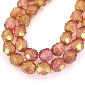 May include: A strand of faceted glass beads in shades of pink and gold. The beads have a metallic sheen and are strung on a clear thread.