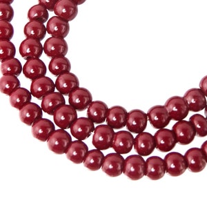 May include: A strand of maroon colored beads, strung together in a circular shape.