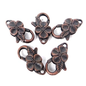 May include: Five antique copper-toned flower-shaped clasps with a leaf design. These clasps are perfect for adding a touch of elegance to jewelry making projects.