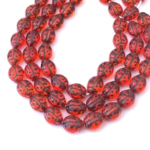 May include: A strand of red glass beads with black ladybug designs. The beads are oval shaped and have a glossy finish.