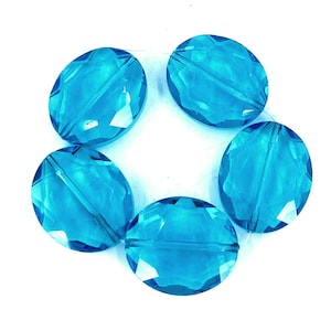 May include: Five faceted, oval-shaped beads in a vibrant turquoise color. The beads are arranged in a circular pattern, each with a central hole for stringing. The transparent beads catch the light, creating a sparkling effect. Ideal for jewelry making.