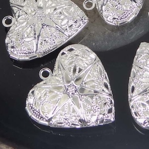 May include: Five silver heart-shaped locket charms with intricate filigree designs. Each charm has a loop at the top for attaching to a necklace or bracelet.