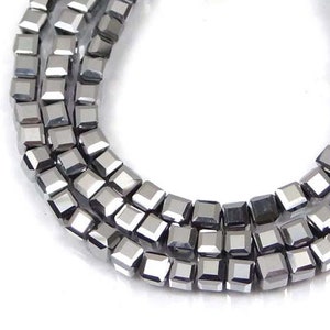 May include: A strand of silver-toned square beads. The beads are faceted and have a metallic sheen.