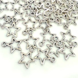 May include: A collection of silver-toned metal star charms, each featuring an open-center design and a small circular loop at the top for attachment. These small, uniform star-shaped components are scattered across the frame in a cluster.