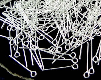 May include: A large pile of silver head pins with small loops on one end. The pins are arranged in a random pattern on a black and white surface.