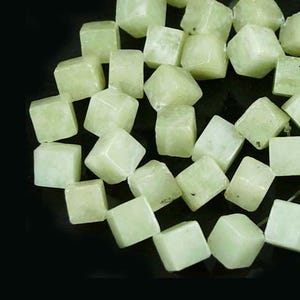 May include: A collection of pale green, cube-shaped gemstones against a black background. The gemstones have a slightly translucent appearance and are scattered across the surface. The overall effect is a display of natural, raw minerals.
