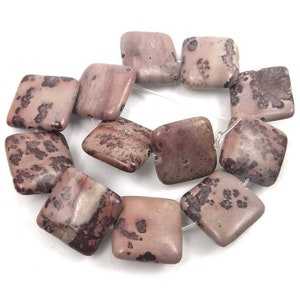 May include: A strand of square-shaped, pink and brown jasper beads with dark brown speckles. The beads are strung on a clear elastic cord.