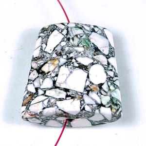 May include: A white, gray, and green terrazzo pendant with a hole for stringing. The pendant is irregularly shaped and has a rough, textured surface.