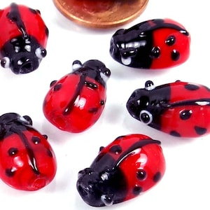 May include: Six red and black ladybug glass beads with black spots. The beads are oval shaped and have a glossy finish.