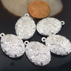 May include: Five silver oval-shaped pendant charms with a filigree design and a star in the centre. The charms have a loop at the top for attaching to a necklace or bracelet.