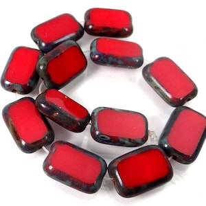 May include: A strand of red glass beads with a mottled, dark blue and green glaze. The beads are rectangular in shape and have a smooth, glossy finish.