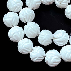May include: A strand of white carved beads, each bead is shaped like a flower. The beads are strung on a black cord and are arranged in a circle.