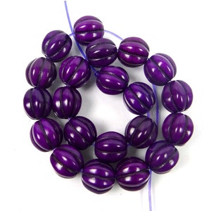 May include: A strand of purple beads with a carved, ribbed texture. The beads are strung on a clear thread.