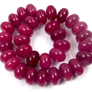 May include: A strand of deep pink, round, gemstone beads. The beads are smooth and polished, with a slight oval shape.