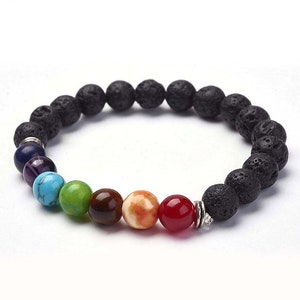 May include: A beaded bracelet featuring a combination of black lava rock beads and colorful gemstone beads. The gemstones are arranged in a rainbow pattern, with colors including red, orange, brown, green, turquoise, purple, and blue. The bracelet is strung on an elastic cord.