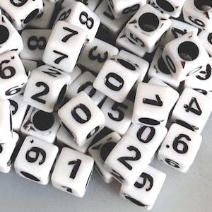 May include: A pile of white plastic cube beads with black numbers on each side. The numbers range from 0 to 9.