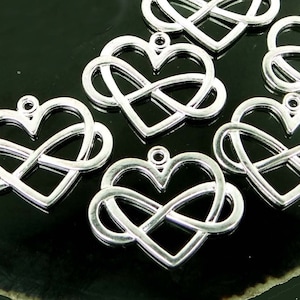 May include: Six silver infinity heart charms, each with a delicate, intertwined design. The charms are arranged on a dark green, textured surface.