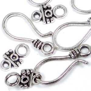 May include: Silver-toned earring hooks with decorative accents. The hooks are made of metal and have a loop at the top for attaching earrings.