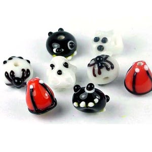 May include: Assortment of Halloween themed glass beads. The beads are black, white, and red with various designs including a spider, ghost, and a pumpkin.