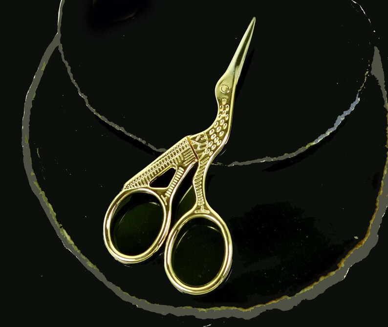 May include: Gold-toned, bird-shaped, decorative scissors with intricate details. The scissors are on a black background.