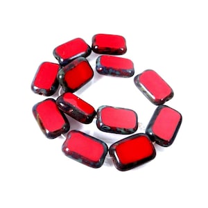 May include: A collection of ten rectangular beads arranged in a loose circular pattern. Each bead features a vibrant, solid red center surface framed by a dark, mottled, and textured border with hints of deep green and black tones throughout.