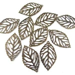 May include: Ten antique gold metal leaf charms with a delicate, intricate design. Each leaf charm has a hole at the top for hanging or attaching to a project.