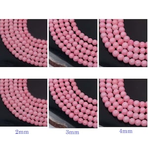 以下が含まれることがあります： 2mm、3mm、4mmのピンク色の丸いビーズ。ビーズは曲線状に配置され、滑らかで磨かれた表面を示しています。画像はビーズのサイズのバリエーションを強調しており、ジュエリー作りに最適です。