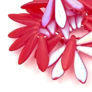 Può includere: Primo piano di una collana di perline rosse e bianche. Le perline sono a forma di petalo e disposte a motivo floreale. La collana ha una finitura lucida ed è su sfondo bianco.