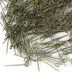 May include: A large pile of gold-toned head pins with a loop at one end. The pins are scattered on a white surface.