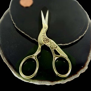 May include: Gold-toned, bird-shaped, small scissors with intricate details on a black and green agate background.