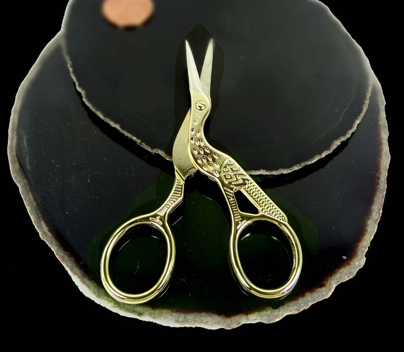 May include: Gold-toned, bird-shaped, small scissors with intricate details on a black and green agate background.
