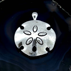 May include: A silver-toned sand dollar charm pendant. The charm is detailed with a five-pointed star design.