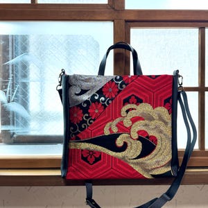 以下が含まれることがあります： 印象的なデザインのトートバッグ。赤い幾何学模様、黒のアクセント、金色の刺繍された波が特徴です。黒いハンドルとショルダーストラップが付いています。バッグのデザインには、花柄と波のモチーフが組み込まれています。