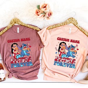 Pu&ograve; includere: Due magliette, una malva e una pesca, ciascuna con una grafica di Lilo e Stitch che mangiano il gelato. Il testo "CUSTOM NAME" e "BESTIE FOREVER" sono stampati sopra e sotto i personaggi.