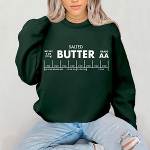 May include: Dark green sweatshirt with white text that reads "SALTED BUTTER AA". The text includes a measurement guide with tablespoons and cup measurements. The net weight is listed as 4 oz (113g).