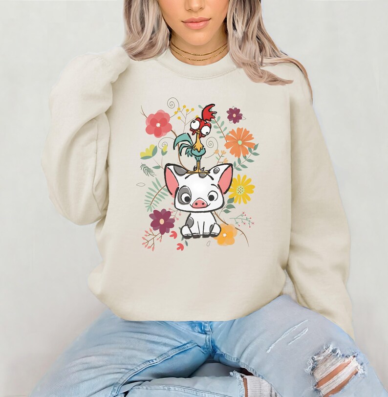 May include: A cream-coloured sweatshirt featuring a cartoon image of a pig and a rooster surrounded by flowers. The pig is white with black spots and the rooster is red, yellow, and green.