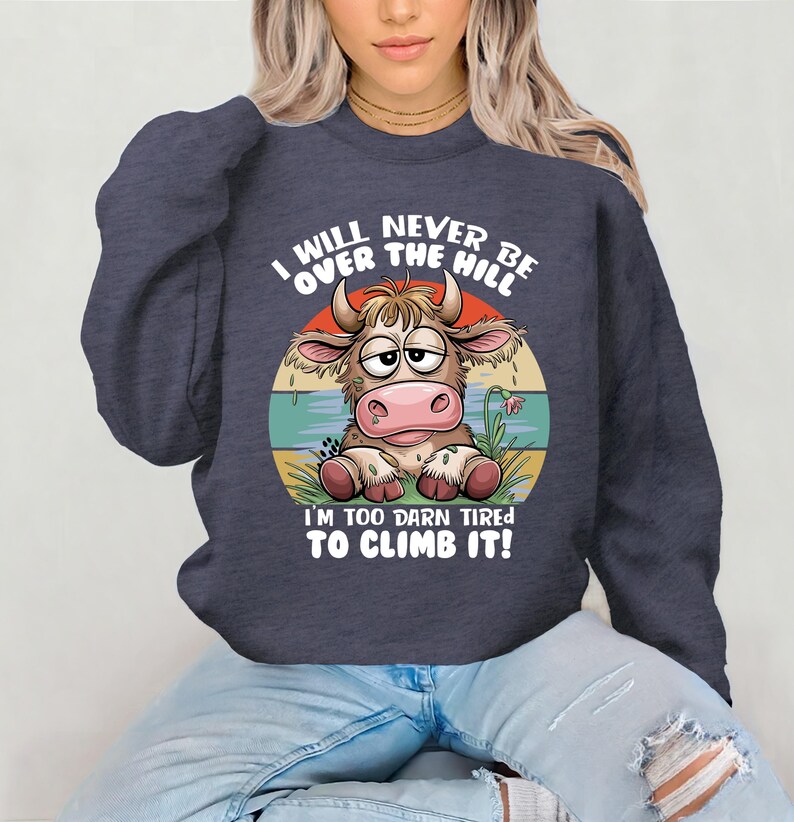 Puede incluir: Una sudadera azul marino con una vaca de dibujos animados y el texto "I will never be over the hill I'm too darn tired to climb it!"