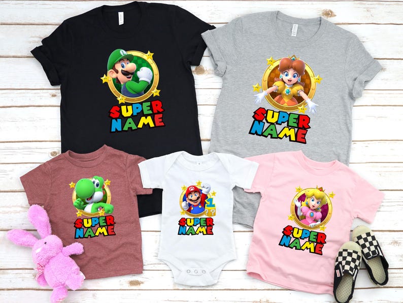 May include: Set of five t-shirts featuring characters from the Super Mario video game franchise. The shirts are in various colors, including black, gray, pink, white, and maroon. Each shirt features a different character, including Mario, Luigi, Peach, Yoshi, and Daisy. The shirts all have the text "SUPER NAME" printed on them.