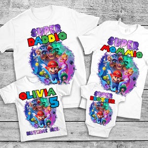 May include: White t-shirts with colorful graphics featuring characters from a video game. The shirts have text that reads "Super Daddio", "Super Mommio", "Olivia 5 Birthday Girl", and "Super Brother".
