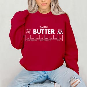 May include: A deep red sweatshirt with white text that reads "SALTED BUTTER AA" and a butter measurement guide. The net weight is 4 oz (113g). The measurement guide includes increments from 1 tbsp to 1/2 cup.