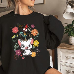 May include: Black sweatshirt featuring a cartoon pig and rooster surrounded by colourful flowers. The pig is white with black spots and the rooster is red, yellow and orange.