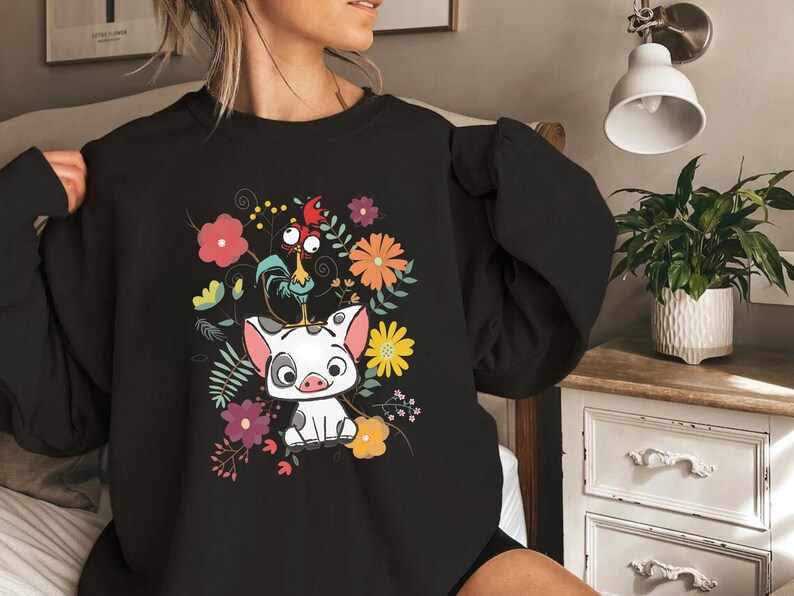 May include: Black sweatshirt featuring a cartoon pig and rooster surrounded by colourful flowers. The pig is white with black spots and the rooster is red, yellow and orange.