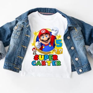 May include: White t-shirt with a colorful graphic of Super Mario, a star, and the text "SUPER CARTER".
