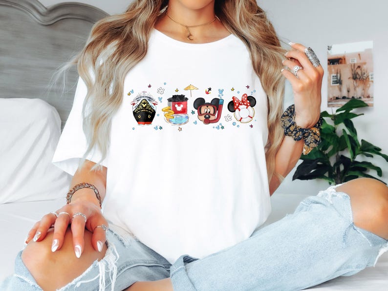 May include: White t-shirt featuring a colourful graphic of Mickey Mouse and Minnie Mouse characters in a boat, a red cup, and a life preserver. The characters are surrounded by stars and other nautical elements.