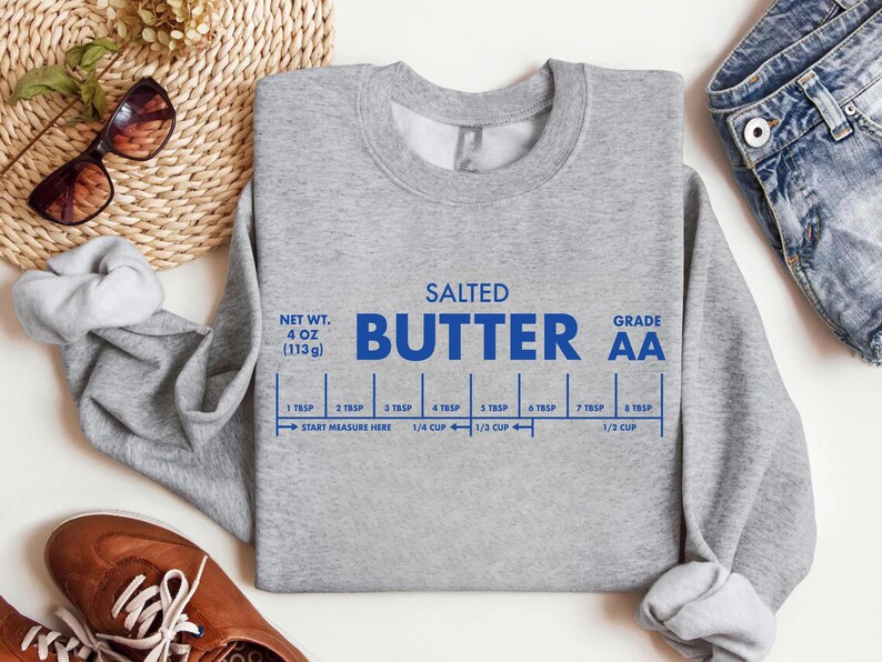 May include: A heather gray sweatshirt with the words "SALTED BUTTER" in blue, along with a measurement guide. The sweatshirt also features the text "NET WT. 4 OZ (113g)" and "GRADE AA".